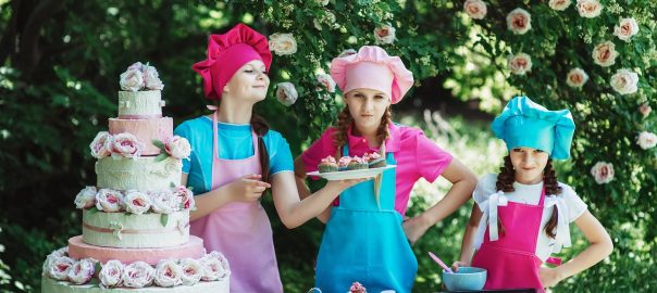 kids in baking aprons and hats alongside table with cake